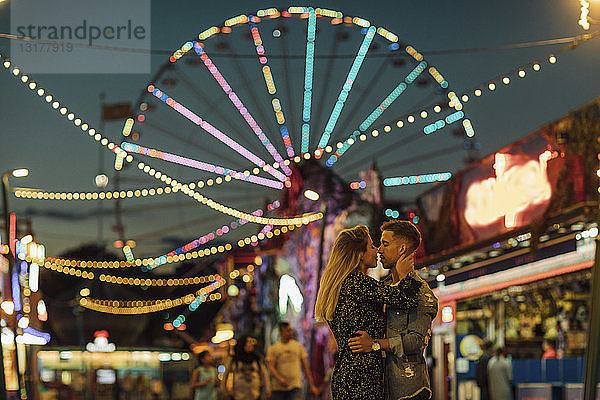 Glückliches junges Paar umarmt und küsst sich auf einer Kirmes