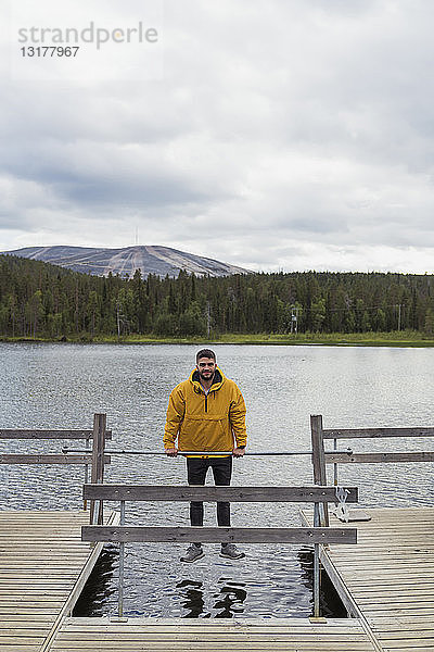 Finnland  Lappland  Mann balanciert auf einer Rute auf einem Steg über einem See