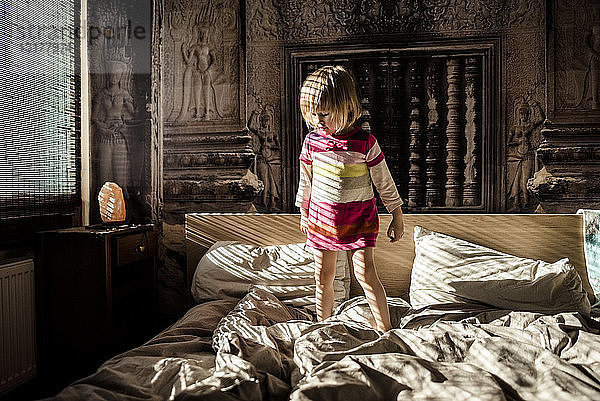 Kleines Mädchen steht zu Hause auf dem Bett der Eltern