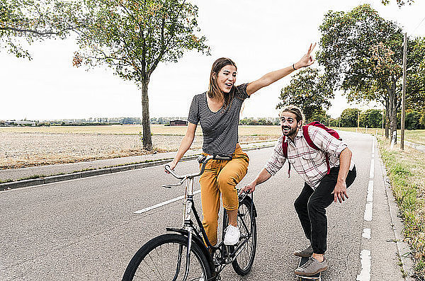 Glückliches junges Paar mit Fahrrad und Skateboard auf der Landstraße