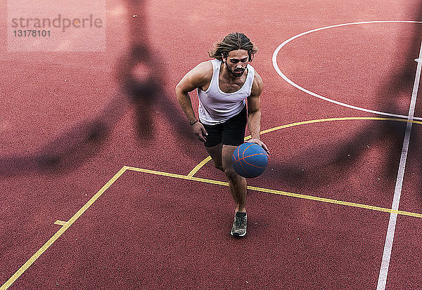 Junger Mann spielt Basketball auf Basketballplatz