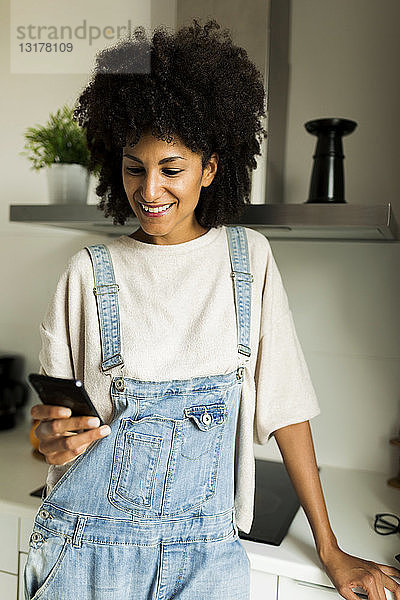 Lächelnde Frau benutzt Mobiltelefon in der Küche zu Hause