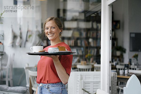 Porträt einer lächelnden jungen Frau  die in einem Cafe Kaffee und Kuchen serviert