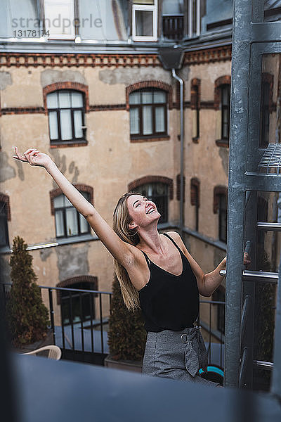 Glückliche junge Frau klettert auf dem Balkon auf eine Feuertreppe