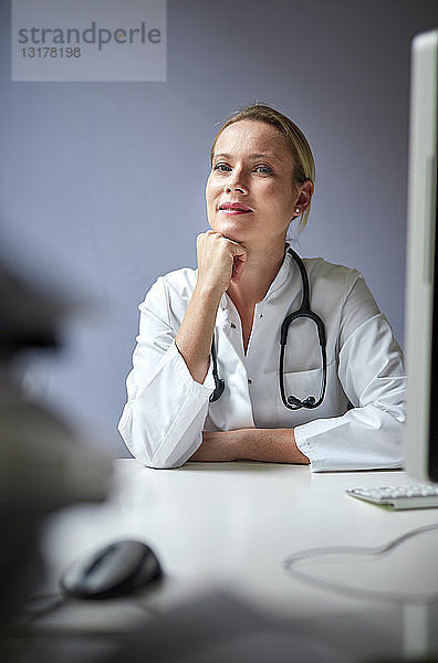 Porträt einer Ärztin mit Stethoskop am Schreibtisch sitzend
