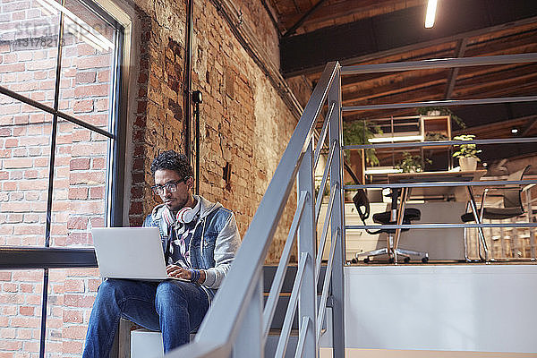 Geschäftsmann sitzt auf der Treppe eines modernen Büros und benutzt einen Laptop