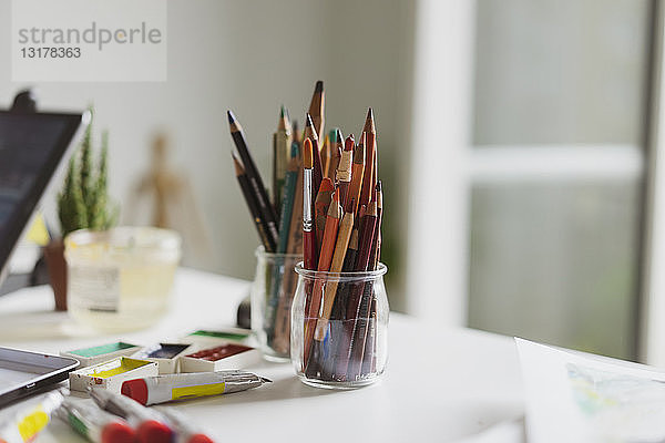 Gläser mit Farbstiften  Farbtuben und Aquarellfarben auf dem Arbeitstisch des Illustrators in einem Atelier