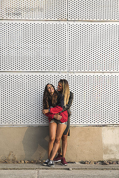 Glückliches lesbisches Paar umarmt sich an einer Wand