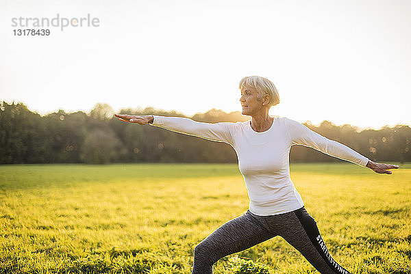 Ältere Frau macht Yoga auf einer ländlichen Wiese bei Sonnenuntergang