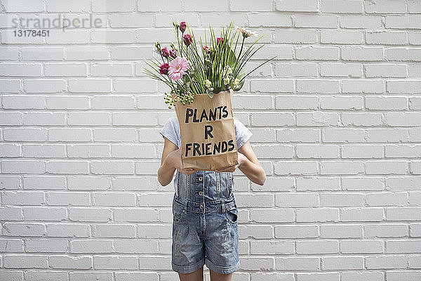 Mädchen versteckt sich hinter Papiertüte mit Blumen