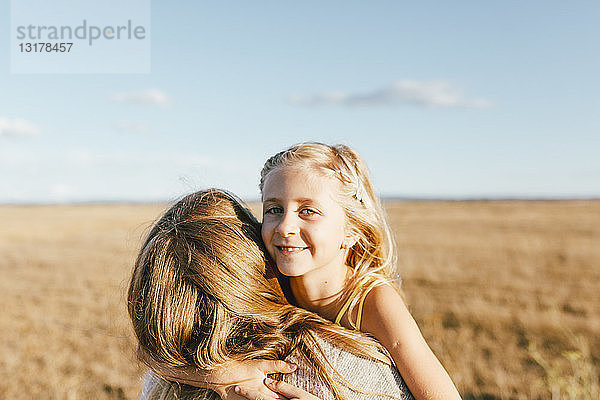 Porträt einer lächelnden Tochter  die ihre Mutter auf einem Feld umarmt