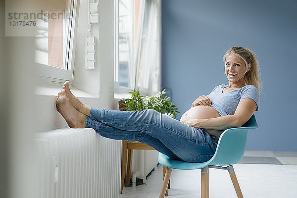 Porträt einer lächelnden schwangeren Frau  die auf einem Stuhl am Fenster sitzt