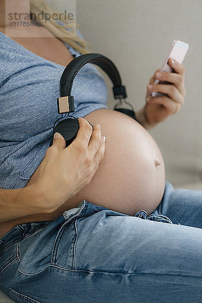Mittelsektion einer schwangeren Frau  die Kopfhörer am Bauch hält
