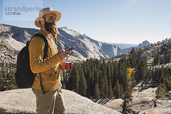 USA  Kalifornien  Yosemite National Park  Wanderer mit Smartphone und Haltebecher