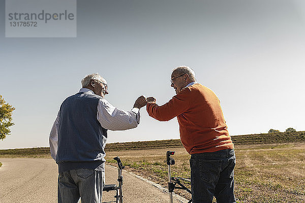 Zwei alte Freunde mit Gehhilfen auf Rädern  Begrüßung auf der Straße