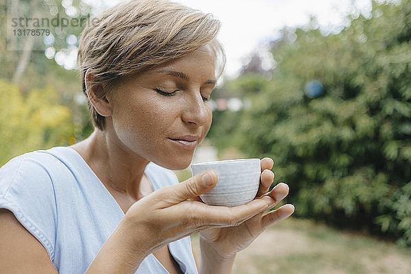 Bildnis einer Frau mit geschlossenen Augen im Garten  die eine Tasse Kaffee hält