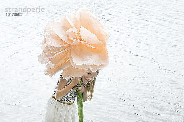 Porträt eines lächelnden blonden Mädchens  das in einem See steht und eine überdimensionale Kunstblume hält