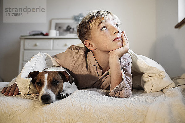 Porträt eines blonden Jungen und seines Jack-Russell-Terriers  die zusammen auf dem Bett liegen