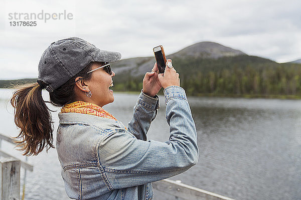 Finnland  Lappland  glückliche Frau auf einem Bootssteg an einem See bei einem Selfie