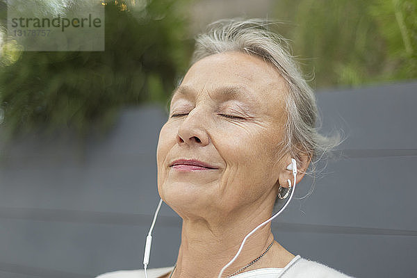 Porträt einer älteren Frau mit geschlossenen Augen  die Kopfhörer im Freien trägt