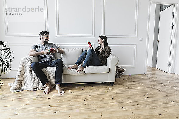Paar  das zu Hause auf der Couch sitzt und sein Smartphone benutzt