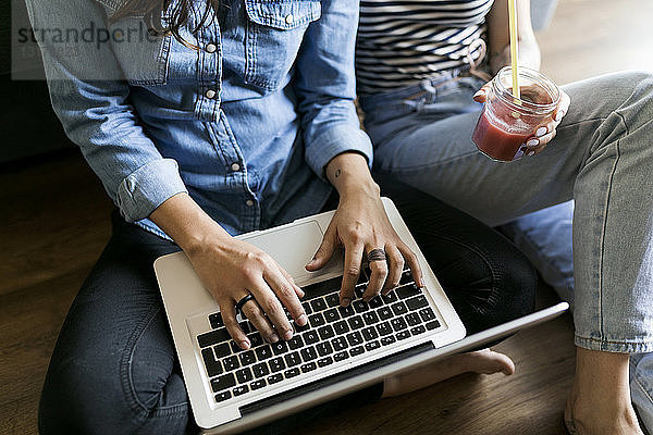 Nahaufnahme von zwei jungen Frauen  die mit Erfrischungsgetränk und Laptop auf dem Boden sitzen