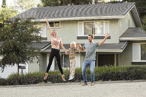 Glückliche Familie mit Sohn springt vor ihrem Haus