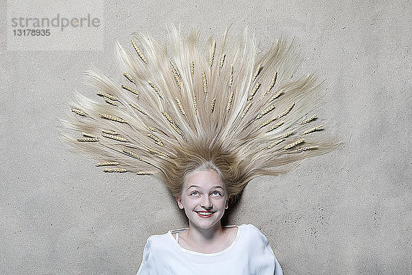 Porträt eines lächelnden Mädchens  das auf dem Boden liegt und Weizenähren auf den Haaren nach oben schaut