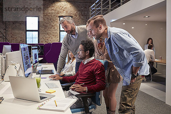 Kollegen schauen einem jungen Mann über die Schulter  der in einem modernen Büro arbeitet