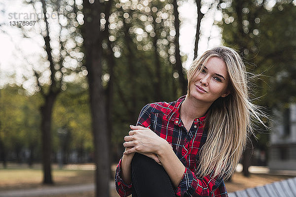 Porträt einer blonden jungen Frau  die im Herbst auf einer Bank sitzt
