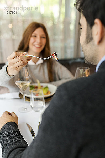 Lächelnde Frau lässt in einem Restaurant den Mann das Essen kosten