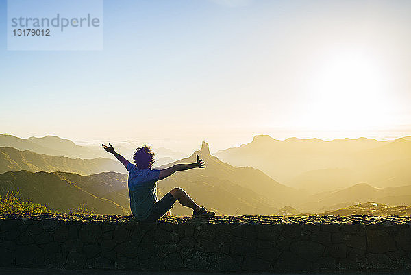 Spanien  Kanarische Inseln  Gran Canaria  Rückenansicht eines glücklichen Mannes  der die Berglandschaft bei Sonnenuntergang betrachtet