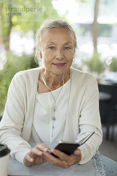 Porträt einer älteren Frau in einem Außencafé mit Mobiltelefon und Kopfhörern