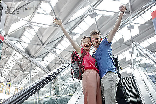 Glückliches Paar jubelt auf der Rolltreppe am Flughafen