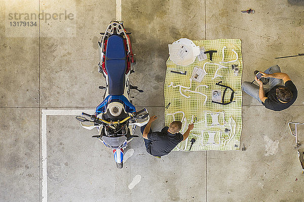 Zwei Männer arrangieren Gegenstände neben dem Motorrad in der Werkstatt