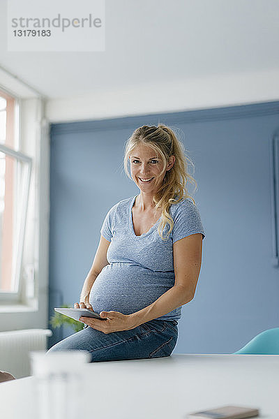 Porträt einer lächelnden schwangeren Frau mit Tablette in der Hand