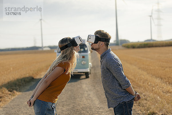 Junges Paar mit VR-Brille küsst sich am Wohnmobil in ländlicher Landschaft