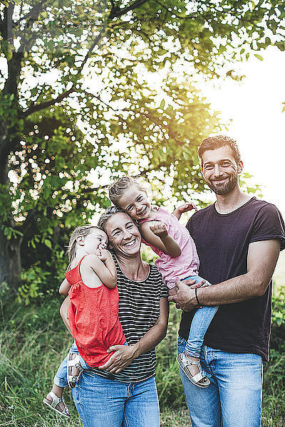 Porträt einer glücklichen Familie mit zwei in der Natur stehenden Töchtern