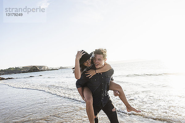 Frankreich  Bretagne  glücklicher junger Mann trägt seine Freundin huckepack am Strand