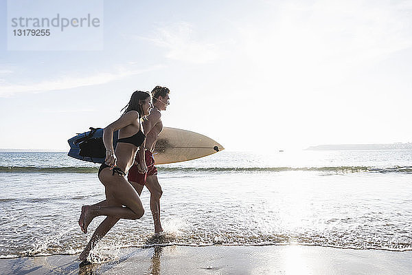 Frankreich  Bretagne  junges Paar mit im Meer laufendem Surfbrett