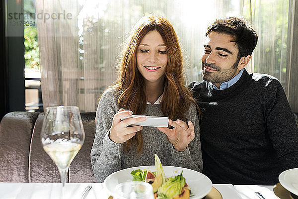 Lächelndes Paar benutzt Handy in einem Restaurant