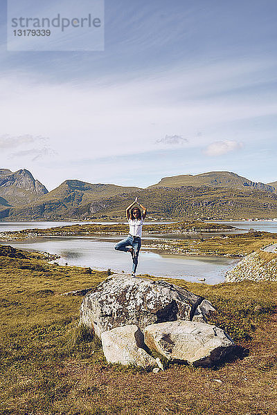 Norwegen  Lofoten  junge Frau steht auf einem Felsen auf einem Bein und macht Yoga