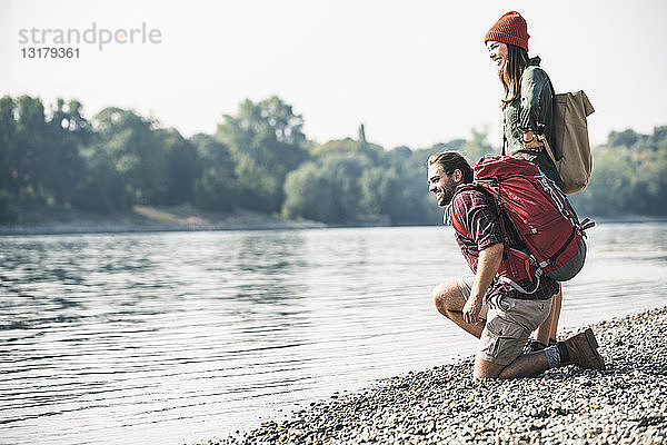 Lächelndes junges Paar mit Rucksäcken am Flussufer