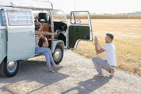 Junger Mann macht Handyfoto von Freundin im Wohnmobil in ländlicher Landschaft