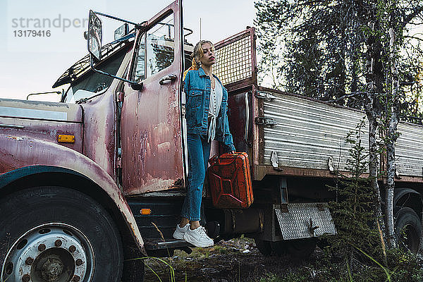 Junge Frau posiert an einem kaputten Oldtimer-LKW  der einen Benzinkanister hält
