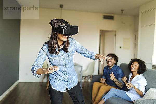 Freunde beobachten Frau mit VR-Brille zu Hause