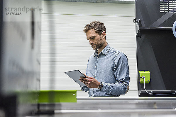 Geschäftsmann in einem High-Tech-Unternehmen  der Produktionsmaschinen mit Hilfe eines digitalen Tabletts steuert