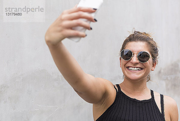 Porträt einer lachenden jungen Frau mit Sonnenbrille  die mit einem Smartphone Selbstgespräche führt