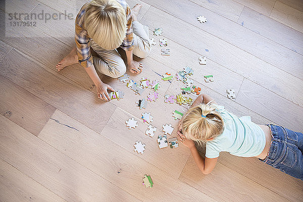 Bruder und Schwester liegen zu Hause auf dem Boden und spielen Puzzlespiele