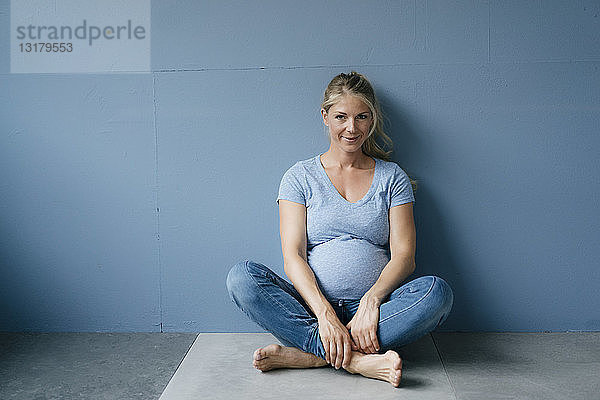 Porträt einer lächelnden schwangeren Frau  die auf dem Boden sitzt